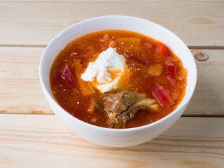 Borsch with sour cream in a white bowl on a wooden background. Side view