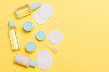 Group of small bottles for travelling on yellow background. Copy space for your ideas. Flat lay composition of cosmetic products. Top view of cream containers with cotton pads