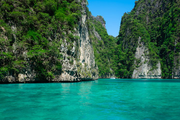 Beautiful turquoise green Pileh Lagoon water with a small white boat in the middle surrounded by steep limestone hills at Phi Phi Island archipelago, Krabi province, Thailand.