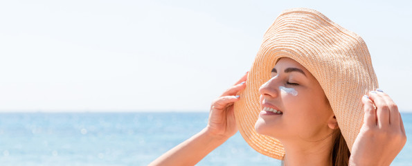 Smiling woman in hat is applying sunscreen on her face. Indian style