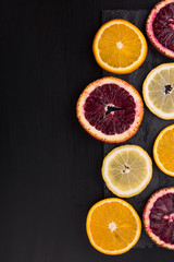 Fototapeta na wymiar Fresh ripe citruses. Lemons, red oranges and oranges on dark stone background. Copy space