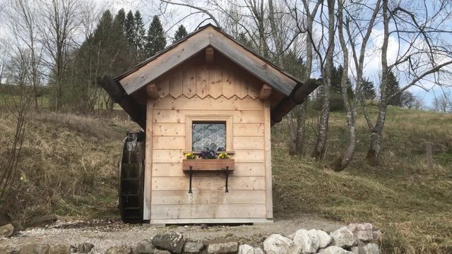 Small water mill in the nature with flower box and bells in the background