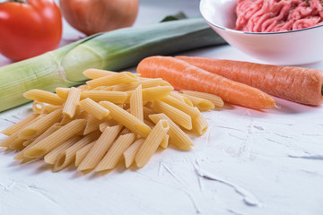 Macaroni, carrot, leak, onion, tomato and meat on white background. Ingredients to prepare pasta bolognese. Raw and healthy products.