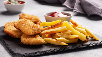 Fried potatoes and chicken nuggets with tomato ketchup sauce. Fast food concept of unhealthy food. Grey concrete table Copy space.