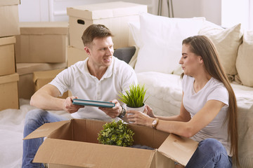 Portrait of happy couple looking at laptop computer together sitting in new house, surrounded with boxes