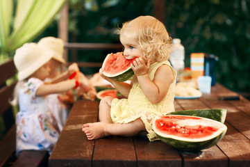 Little blonde girl eating a juicy watermelon in the garden. Children eat fruit on the street. Healthy food for children. Toddler gardening.