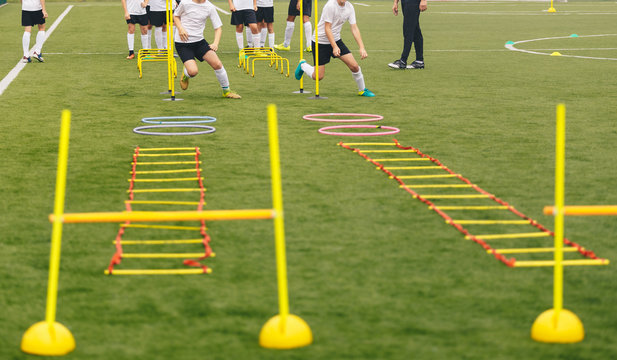 Soccer field with training equipment and players with coach in background. Junior football team training and coach. Sport team on training. Football training equipment: ladder, hula hoop, hurdle, cone