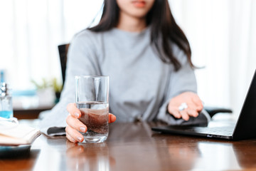 Businesswomen working at home with glass of water takes white round pill in hand.