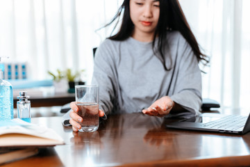 Businesswomen working at home with glass of water takes white round pill in hand.