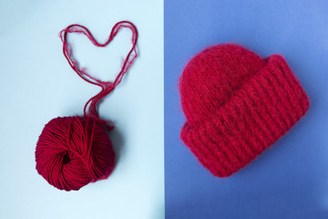 Obraz na płótnie Canvas Knitted red hat on the two colors background. Blue background. Knitting courses. Online education. Flat lay. Top view. Place for text and design. Copy space. Knitting with love. Quarantine life. The h