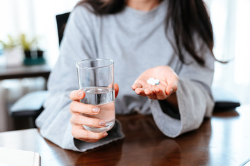 Businesswomen working at home with glass of water takes white round pill in hand.