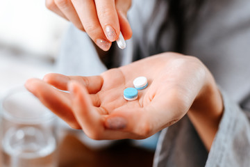 Businesswomen working at home with glass of water takes white round pill in hand.