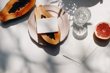 Summer stationery still life scene. Glass of water, cut papaya fruit and grapefruit. White table...