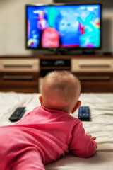Girl infant lying on bed and watching cartoons on tv screen