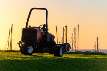 Maintenance works with lawn mower of evergreen grass field on large golf course and yacht club marina on Tenerife island, Canary, Spain