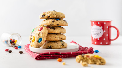 Cookies with colorful candies and chocolate chips and a mug of cocoa on white background. Side view. Multicolor biscuits for holidays.