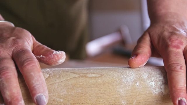 Rolling out the raw dough on a wooden board covered with flour with a rolling pin close up motion