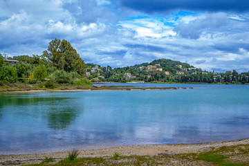 Beautiful summer landscape with sea bay with calm water, village and mountains on the horizon and clouds on blue sky. 