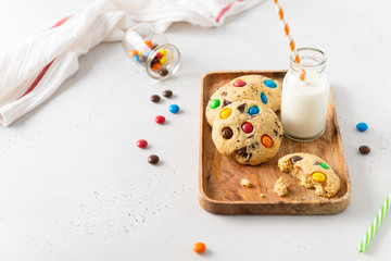 Homemade cookies with multi colored candy and chocolate chips, served with glass of milk on white background. Copy space. Holiday background, greeting card. Bakery, confectionery, cookbook recipe