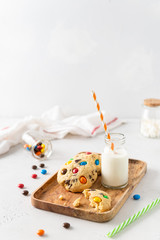 Cookies with colorful candies and chocolate chips and a bottle of milk on white background. Side view, copy space. Multicolor biscuits for holidays. Cooking book recipe, children menu