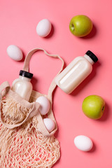 Obraz na płótnie Canvas Milk, eggs, apples and a shopping bag on a pink background