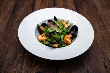 Healthy salad. Lettuce leaves with seafood: mussels and king prawns in a plate on a wooden table.