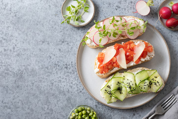 Sandwiches with fresh vegetables, radishes, tomatoes, cucumbers and microgreens on grey. View from above. Copy space.