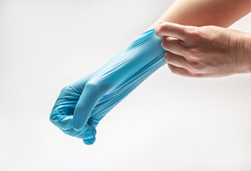 Woman puts on a latex blue medical glove on a white background. Pulls on one hand in a fist. Horizontal orientation