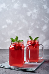 Homemade strawberry tea with mint in mason jar on gray concrete table background, copy space. Cold summer berry drink in sparkling glasses. Fresh vitamin beverage