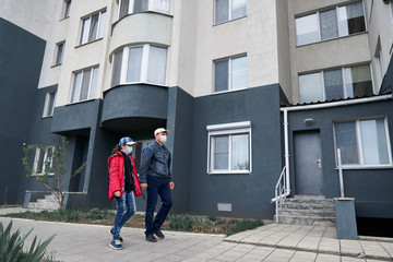 man and child girl walks near wall of high-rise buildings with apartments, father and daughter, a residential area, a medical mask on their faces protects against viruses and dust