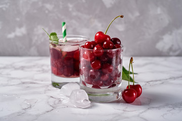 Fresh cherry lemonade with ice, mint and paper straw in sparkling glasses on table, copy space. Cold summer drink. Berry cocktail