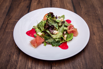 Red beef carpaccio in a white plate and lettuce leaves salad with Blue cheese on a wooden table.