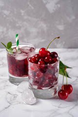Fresh cherry lemonade with ice, mint and paper straw in sparkling glasses on table, copy space. Cold summer drink. Berry cocktail
