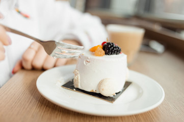 Young woman`s hands with a fork cutting off a piece or creamy parfait cake with raspberry and blackberry on top