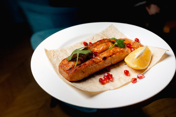 A piece of tasty grilled salmon steak on Pita served with lemon and garnet grains
