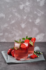 Fresh strawberry lemonade with ice, mint and paper straw in sparkling glasses on gray table background, copy space. Cold summer drink. Berry cocktail