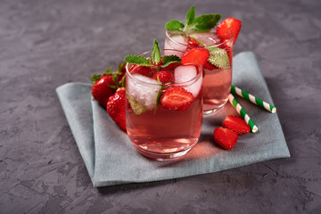 Fresh strawberry lemonade with ice, mint and paper straw in sparkling glasses on gray table background, copy space. Cold summer drink. Berry cocktail
