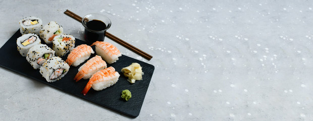food delivery set of sushi and rolls with salmon and shrimp on a gray table next to a laptop. lunch at the computer. the concept of smart office. Top view of sushi, uramaki, hosomaki and nigiri. 