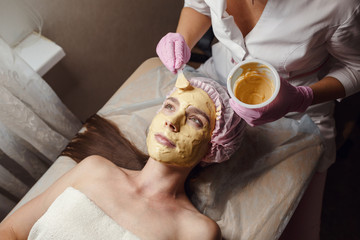 cosmetology specialist applying gold facial mask using brush