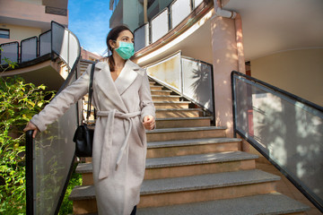 Donna vestita con un cappotto chiaro e una mascherina protettiva sesce fuori casa dal suo palazzo