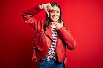Young beautiful brunette woman wearing casual jacket standing over red background smiling making frame with hands and fingers with happy face. Creativity and photography concept.