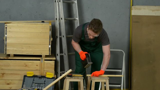 A man uses an electric saw to cut wooden planks.