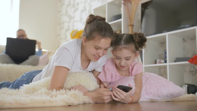 Two teenage girls lying on the floor in the living room and watch something interesting on your smartphone.