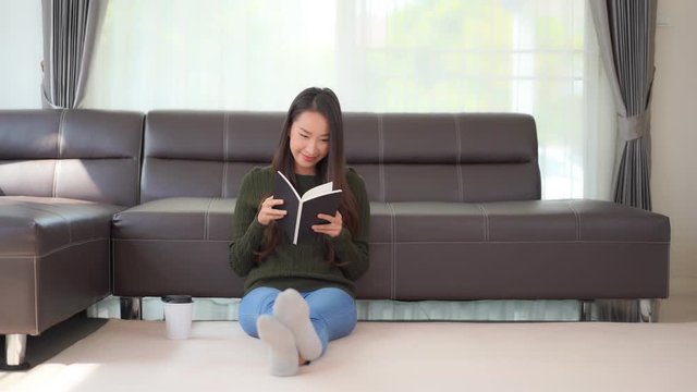 Spending time at home with a good book, a young, Asian, woman sits on the floor with a hot drink and reads.