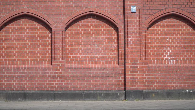 Cool man / athlete wheelies and balances with BMX Bike next to red urban building background with bricks / Slowmo / Outdoor Extreme & Action & Fun Sports
