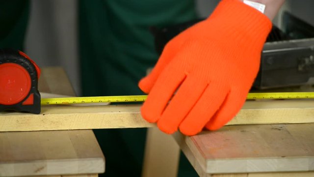A man wearing gloves makes a mark on the board with a pencil and a tape measure.