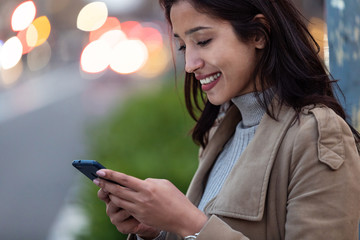 Pretty young woman using her smartphone while standing in the street.