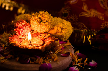 shining terracotta lamp with flowers and rose petals against dark red golden background. festivity concept.