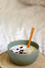 Breakfast bowl with oatmeal, berries, chia seeds and coconut chips on a bed with floral sheets. Selective focus.