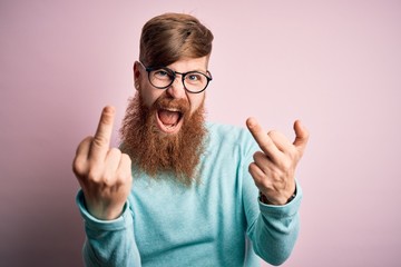 Handsome Irish redhead man with beard wearing glasses over pink isolated background Showing middle...